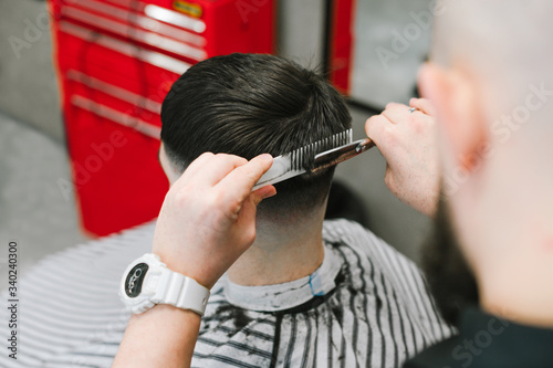 Professional barber cuts a client with dark hair with scissors and a comb. Creating a stylish hairstyle in a barbershop. Close-up photo. Background.