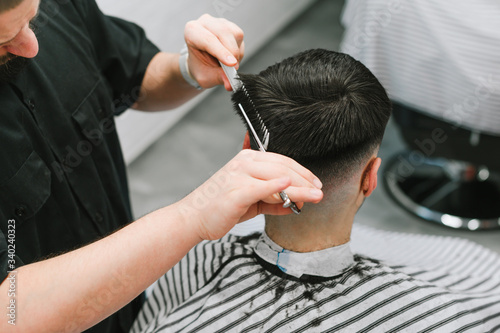 Closeup photo, male hairdresser clipping client's hair with scissors. Barber trims a man in a light barber shop, use scissors. Men's haircut concept. © bodnarphoto