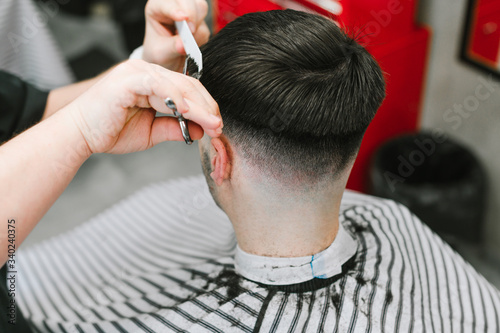 Closeup photo, professional barber's hands trimming brunette man's hair, creating fashionable haircut with scissors. Black-haired client cuts her hair in a barber shop. Background