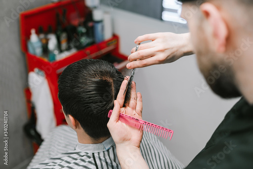Professional male haircutter cuts the client's hair with scissors and comb in a barber shop. Creating a trendy male hairstyle with scissors in a men's hairdresser. Closeup