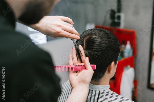Male hairdresser cuts a brunette client's hair in a barber shop, uses scissors and a comb. Process of creating a stylish hairstyle in a men's hairdresser, close photo.
