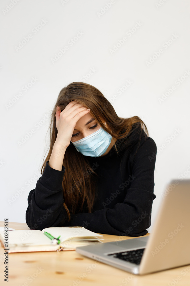 woman girl wearing a protective mask with a high fever and headache, works with a laptop during quarantine coronavirus,