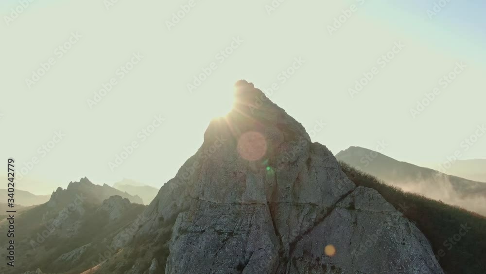 AERIAL mountain range in autumn sun beams and glare against the top at the foot of the mist