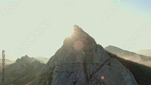 AERIAL mountain range in autumn sun beams and glare against the top at the foot of the mist
