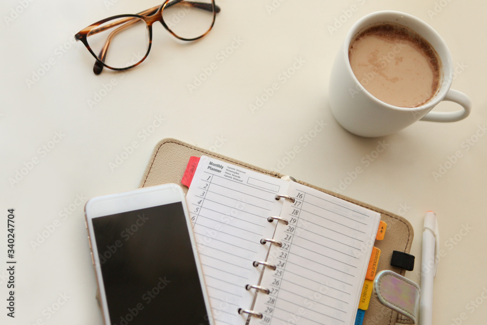 Day planner noter with Mobile phone and notes paper. cozy working place at home. stylish interior in warm pastel colors, table and white coffee mug with glasses. stay home - a place for home office Day planner noter with Mobile phone and notes paper. cozy working place at home. stylish interior in warm pastel colors, table and white coffee mug with glasses. stay home - a place for home office
