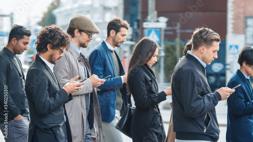 Office Managers and Businessmen are Walking in Front of a Modern Glass Office Building and Use Their Smartphones. People are Dressed Smartly and Look Successful. They are Occupied by Their Devices.
