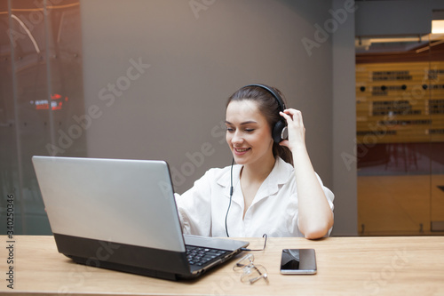 Lifestyle portrait in the interior. A young woman with headphones works at a laptop