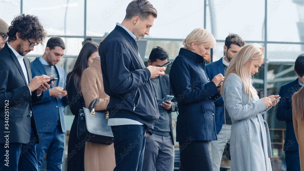 Obraz premium Office Managers and Businessmen are Standing in Front of a Modern Glass Office Building and Use Their Smartphones. People are Dressed Smartly and Look Successful. They are Occupied by Their Devices.