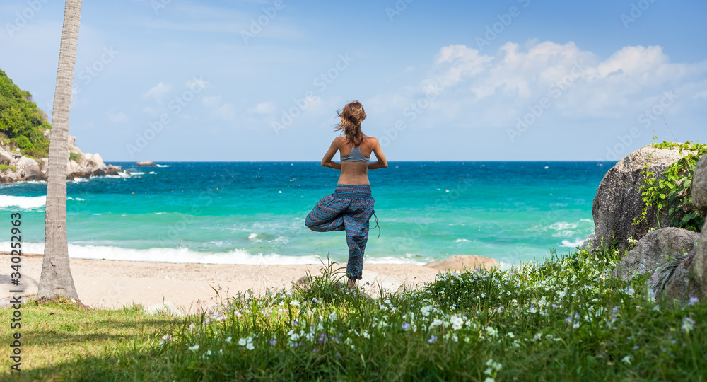 Young woman performs yoga exercises on a green lawn with sea on the background