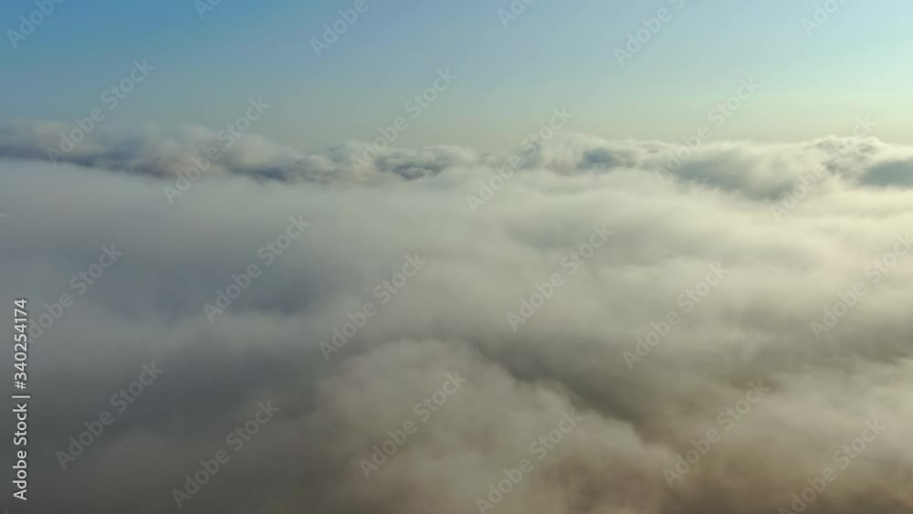 Flying over a dense layer of white clouds that are illuminated by the bright sun under the blue sky Flying over a dense layer of white clouds that are illuminated by the bright sun under the blue sky