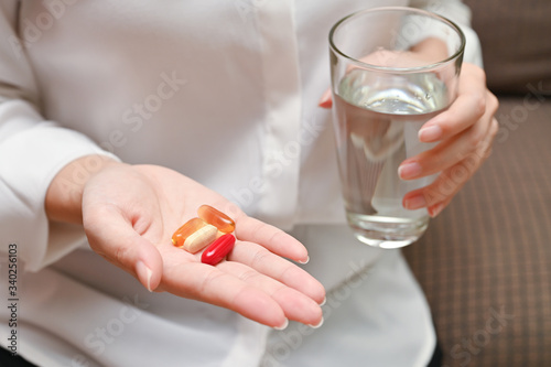 Close up Asian woman holding pill and a glass of water sitting on sofa. Concept of taking daily medicine, Multivitamins and supplements and medicine to cure head ache, stomach pain sedation meds.