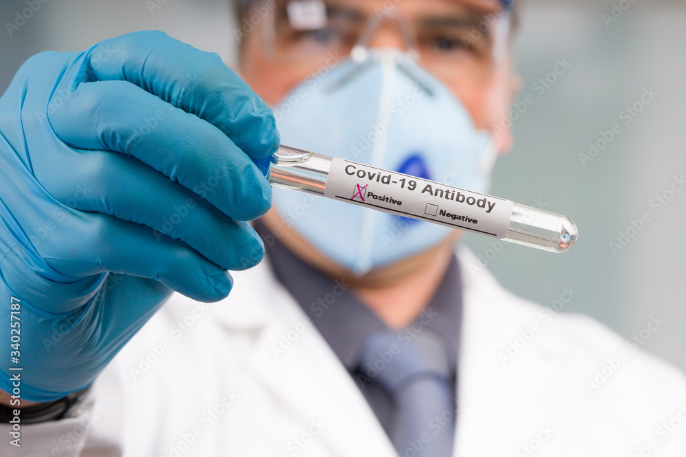 Scientist or doctor with medical face mask and medical gloves shows a virus test tube with result markers in front of laboratory in background Scientist or doctor with medical face mask and medical gloves shows a virus test tube with result markers in front of laboratory in background