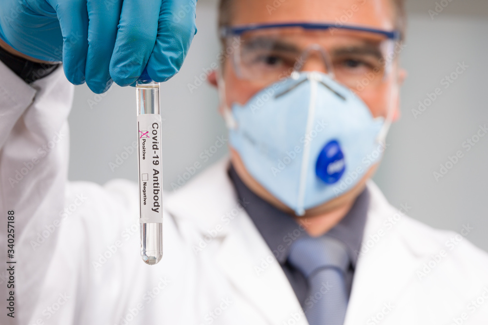 Scientist or doctor with medical face mask and medical gloves is handling virus test tube with antobody result markers in front of laboratory in background Scientist or doctor with medical face mask and medical gloves is handling virus test tube with antobody result markers in front of laboratory in background