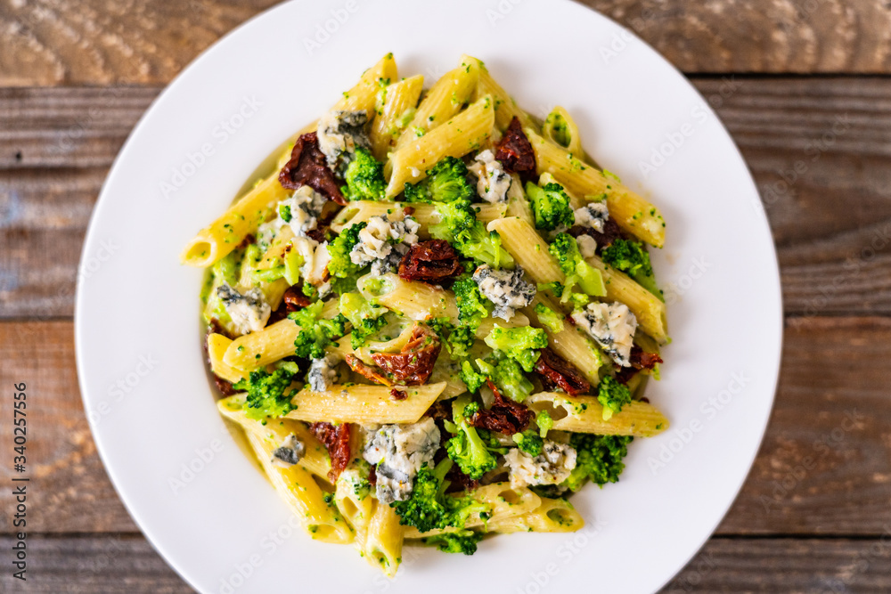 Penne with gorgonzola broccoli and sun-dried tomatoes on wooden table Penne with gorgonzola broccoli and sun-dried tomatoes on wooden table