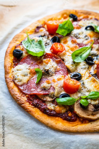 Pizza with pepperoni gorgonzola and champignons on baking paper 