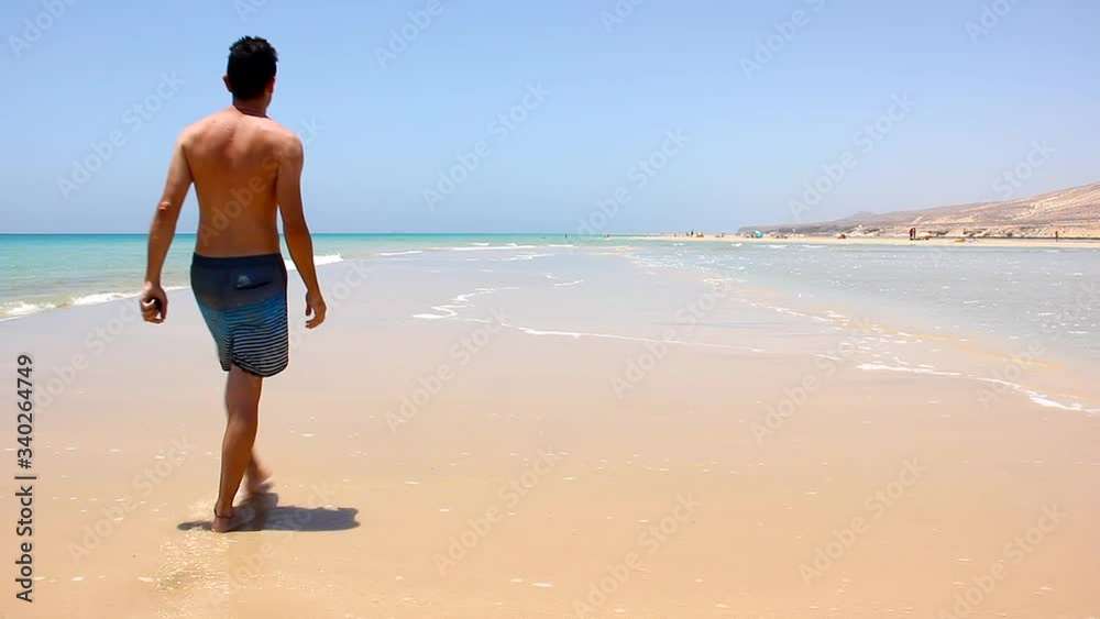 Young man walking alone at empty Sotavento beach in Fuerteventura. Lonely male tourist enjoying summer vacation at Jandia coast in Canary Islands. Holidays destination, healthy lifestyle concepts Young man walking alone at empty Sotavento beach in Fuerteventura. Lonely male tourist enjoying summer vacation at Jandia coast in Canary Islands. Holidays destination, healthy lifestyle concepts