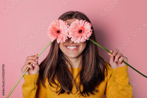 Young woman dressed in yellow sweater with  bouquet of  gerberas on pink background photo