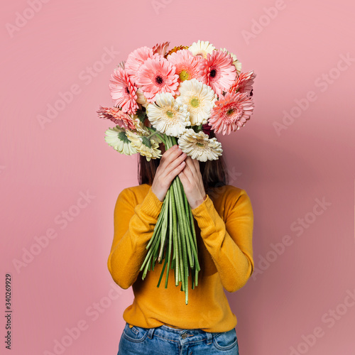 Young woman dressed in yellow sweater with  bouquet of  gerberas on pink background photo