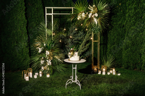 night wedding ceremony, the arch is decorated with flowers, candles and garlands of light bulbs and there is a wedding cake on the table