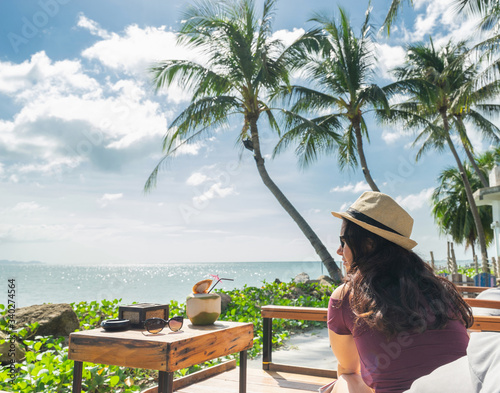 Woman in hat relaxing on bean bag in beach cafe. Blue sea and palms on background. Travel concept. © upslim