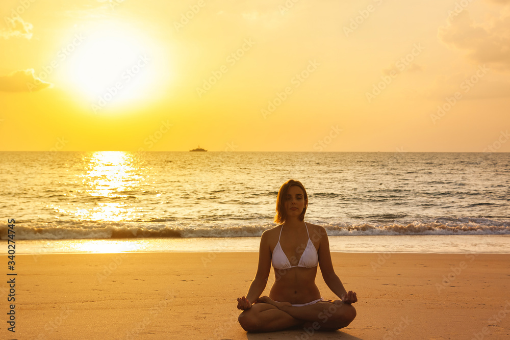 Meditation yoga woman on the beach with background of the sea and sunset. Healthy lifestyle.