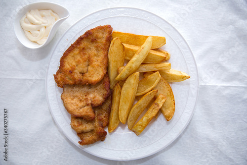 Fried chicken cutlet. Fry the potatoes in a white plate . Red Dry Pepper in Traditional Basket . Mayonnaise inside a bowl .