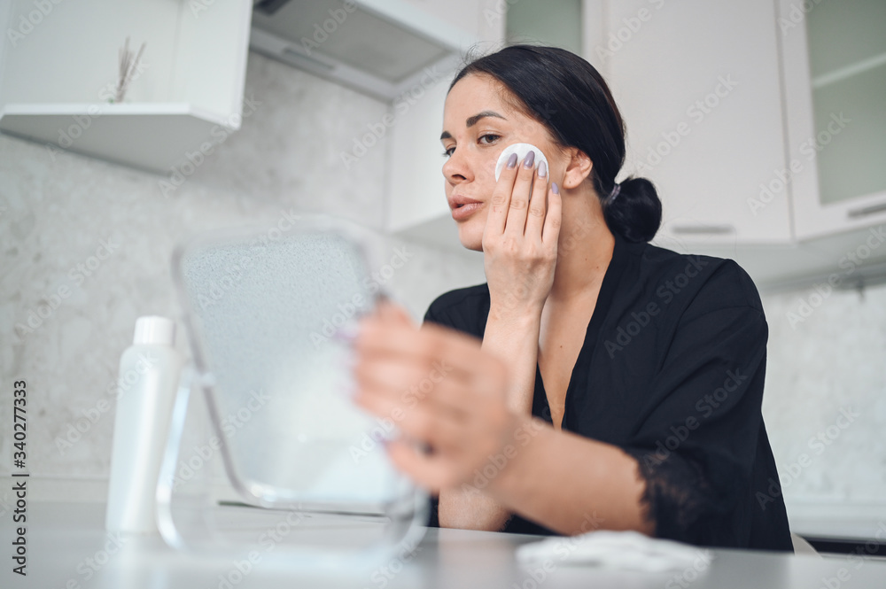 Beautiful brunette woman removing makeup from her face with mirror. Cute beautiful natural beauty girl cleaning face with cotton sponge. Cosmetology and spa, problem skin care, acne treatment concept Beautiful brunette woman removing makeup from her face with mirror. Cute beautiful natural beauty girl cleaning face with cotton sponge. Cosmetology and spa, problem skin care, acne treatment concept