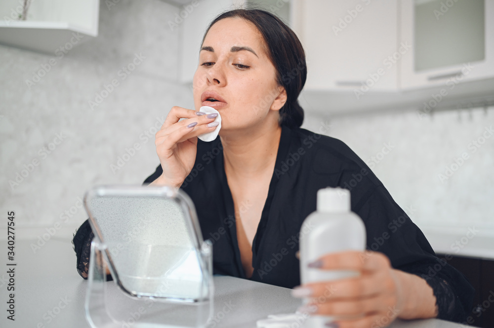 Beautiful brunette woman removing makeup from her face with mirror. Cute beautiful natural beauty girl cleaning face with cotton sponge. Cosmetology and spa, problem skin care, acne treatment concept Beautiful brunette woman removing makeup from her face with mirror. Cute beautiful natural beauty girl cleaning face with cotton sponge. Cosmetology and spa, problem skin care, acne treatment concept