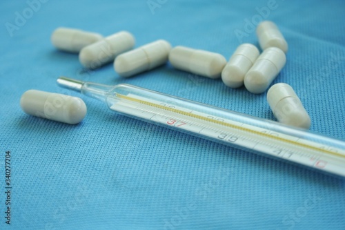 Mercury thermometer with tablets on blue background. Instruments necessary for cold and flu. Coronavirus concept.