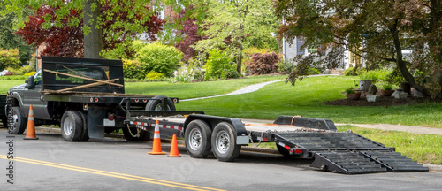 Landscaping truck with empty flatbed trailer with ramp parked on residential neighborhood street. photo