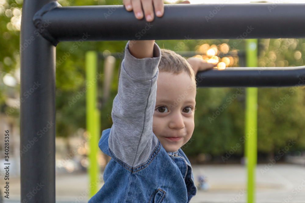 Happy small boy hanging on brachiating bar at a school yard. Selective focus. Happy small boy hanging on brachiating bar at a school yard. Selective focus.