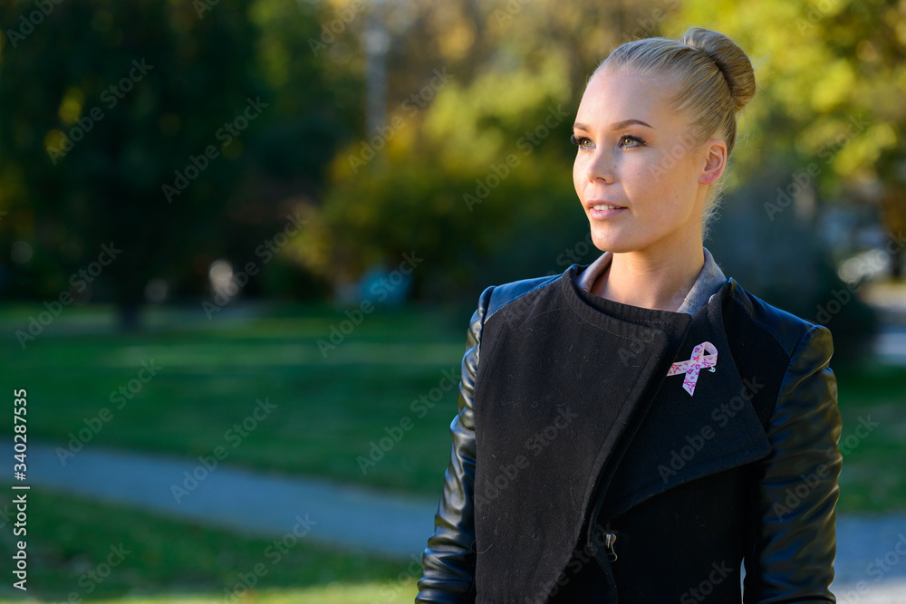 Young happy woman smiling and thinking while wearing pink ribbon for symbol of breast cancer awareness