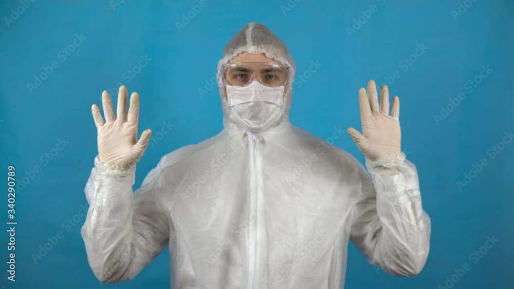 Young man in a protective suit. A man shows sterile hands in gloves on a blue background. Protection against virus outbreaks. Young man in a protective suit. A man shows sterile hands in gloves on a blue background. Protection against virus outbreaks.