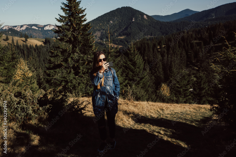 Girl standing on mountain and take pictures on the phone during a hiking trip, the concept of freedom. Travel adventure woman taking photo on smart phone on mountain enjoying beautiful nature.