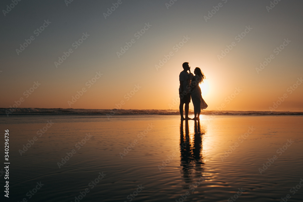 girl and guy stand at sunset by the ocean