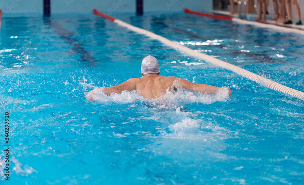 Swimming pool athlete training indoors for professional competition. Teenager swimmer wearing white swimming cap performing the butterfly stroke
