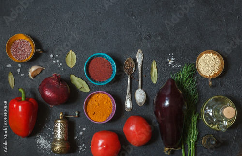 Fresh vegetables and spices in multicolored dishes on a black background, top view with space