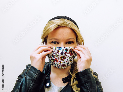 Young blonde caucasian woman wearing colorful face mask made of fabric isolated infront of white background