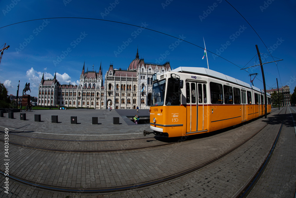 A wide angle view of the east side of the Hungarian Parliament Building with the yellow line train and riders