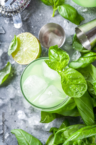 Basil smash gin alcoholic cocktail. Long alcohol drink recipe with fresh basil leaves and limes, grey stone background copy space