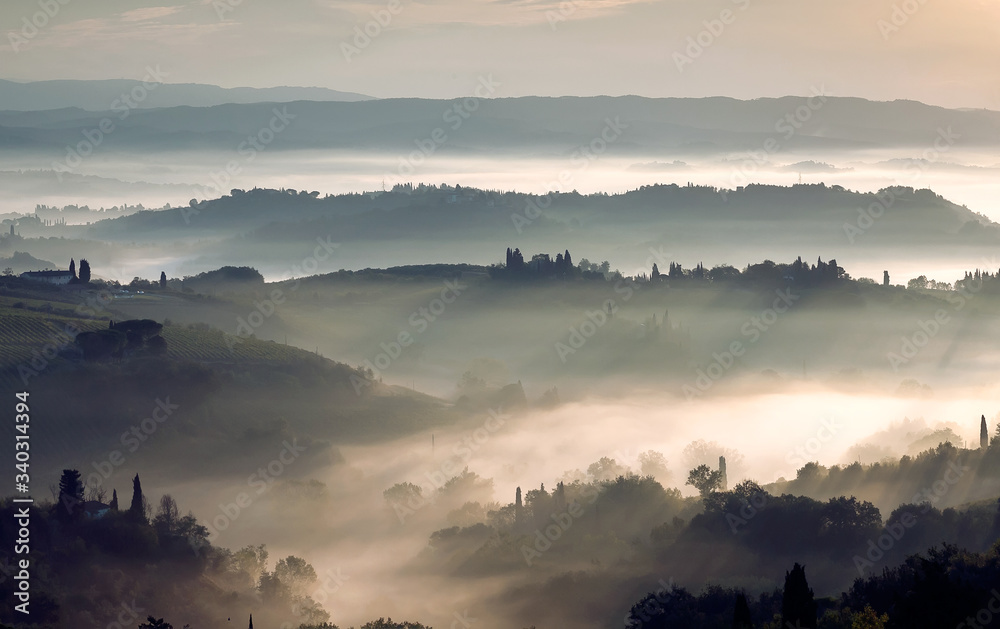 Sunrise over grenn hills of Italy. Misty morning over rural landscape with gardens, farms, trees, fields in Tuscany province.