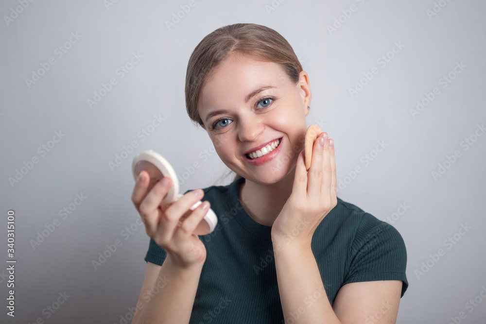 Young Caucasian woman girl is putting her make up powder foundation with funny face expression Young Caucasian woman girl is putting her make up powder foundation with funny face expression