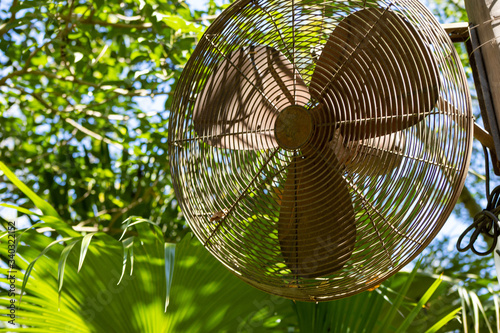A rusted oscillating fan high on a post on a sunny day