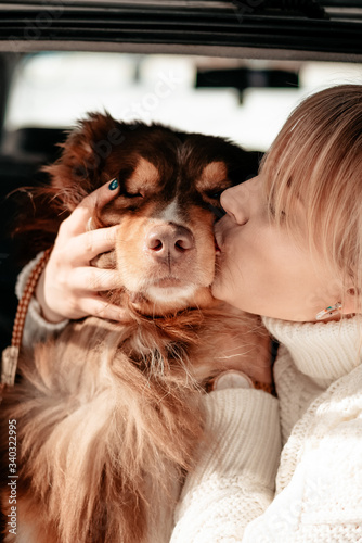Beautiful woman kiss and cuddle with a dog breed Lassie Australian Shepherd in the trunk of a car. Caring for a dog. Dog is a mans friend  a true friend. Sunny winter day.