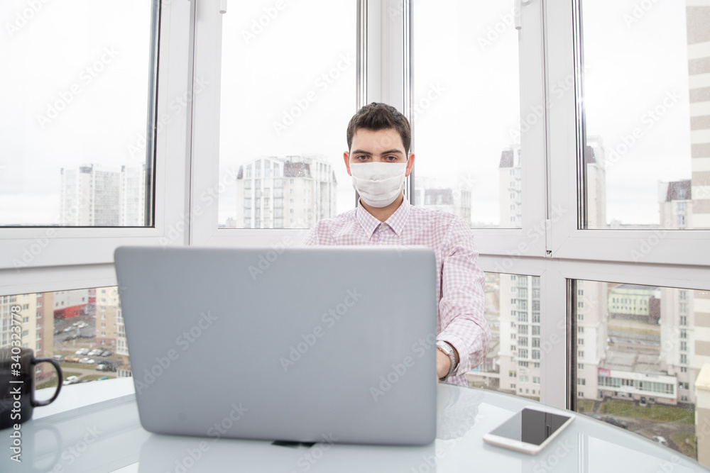 A guy in a protective face mask works at a computer from home during a virus epidemic. Quarantine during viral infection A guy in a protective face mask works at a computer from home during a virus epidemic. Quarantine during viral infection