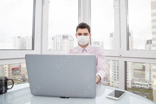 A guy in a protective face mask works at a computer from home during a virus epidemic. Quarantine during viral infection © makedonski2015
