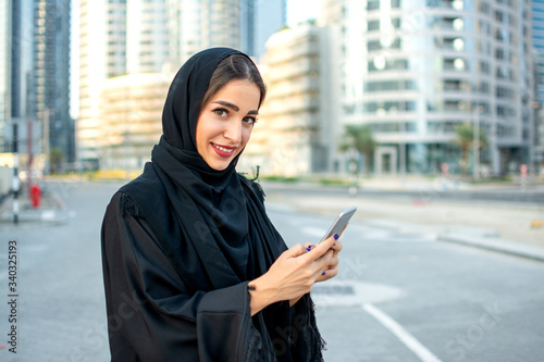 Schilderij op canvas Beautiful smiling young Muslim woman using smartphone on the street