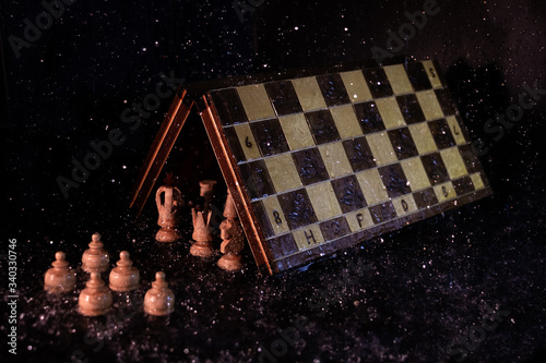 Main chess figures under the game board protecting themselves from the rain in front of the pawns under it, in a dark environment photo
