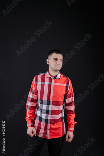 young guy in a plaid shirt posing on a black background photo studio