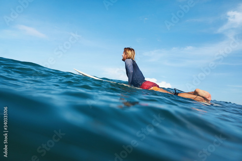 Surfing. Portrait Of Young Surfer In Wetsuit On Surfboard. Handsome Man Swimming In Ocean. Waved Water Surface, Blue Sky With Soft Clouds On Background.